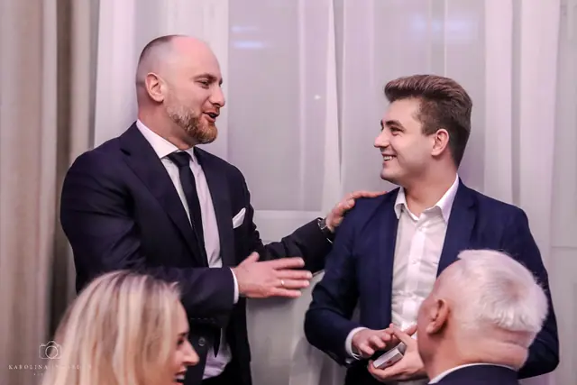 Oferta: iluzjonista na sylwestra. Iluzjonista Bartosz Rybczyński z uczestnikiem pokazu przy stole na imprezie firmowej